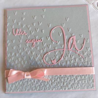 Einladungskarte zur Hochzeit in grau/rosa, mit geprägtem Hintergrund, und "wir sagen Ja" Schriftzug
