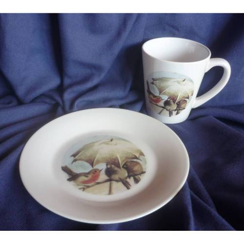 Tasse und Frühstücksteller mit Rotkehlchen und anderen Vögeln unterm Regenschirm